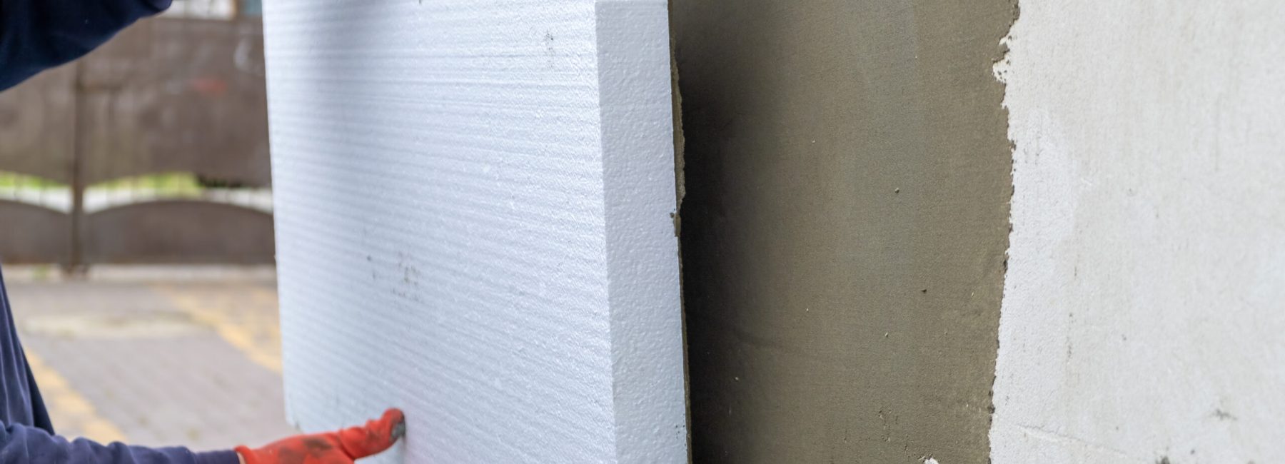 Construction worker installing styrofoam insulation sheets on house facade wall for thermal protection.